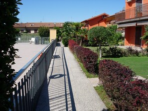 A pathway leading to a building with a balcony, surrounded by greenery and a clear sky. - Da Elena Apartment, two-room apartment with private garden, complex with pool and tennis court (Pacengo)