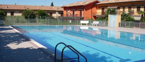 Une piscine dotée d’une terrasse carrelée, de garde-corps en métal et d’un banc.