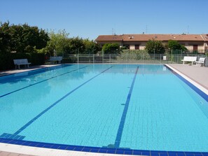 A rectangular swimming pool with clear blue water, surrounded by a metal fence, benches, and greenery. - Da Elena Apartment, two-room apartment with private garden, complex with pool and tennis court (Pacengo)