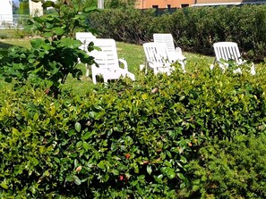 A garden area with white lounge chairs and dense green foliage. - Da Elena Apartment, two-room apartment with private garden, complex with pool and tennis court (Pacengo)