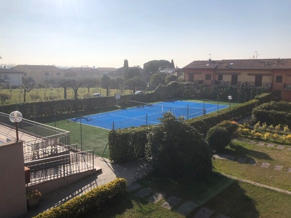 A tennis court surrounded by well-maintained hedges and a building with a satellite dish. - Da Elena Apartment, two-room apartment with private garden, complex with pool and tennis court (Pacengo)