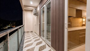 A balcony with a chevron-patterned floor, a glass door, and a view of the city at night. - Aarambh Hillside View (Dehradun)