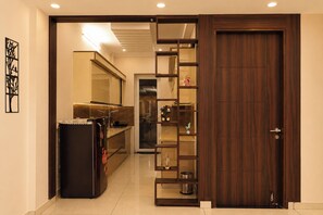 A hallway with a sliding door leading to a room, a refrigerator, and a shelf with decorative items. - Aarambh Hillside View (Dehradun)