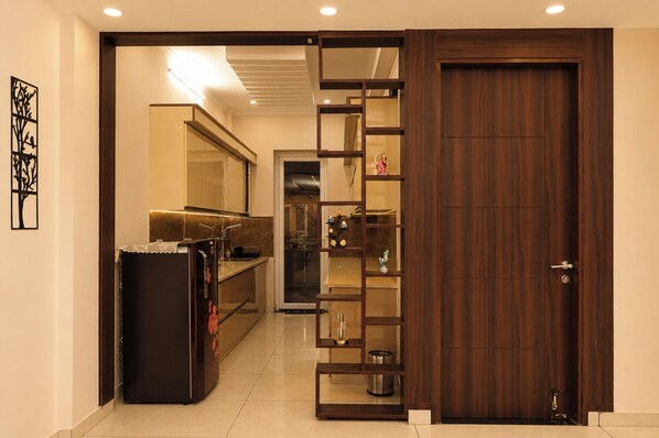 A hallway with a sliding door leading to a room, a refrigerator, and a shelf with decorative items. - Aarambh Hillside View (Dehradun)