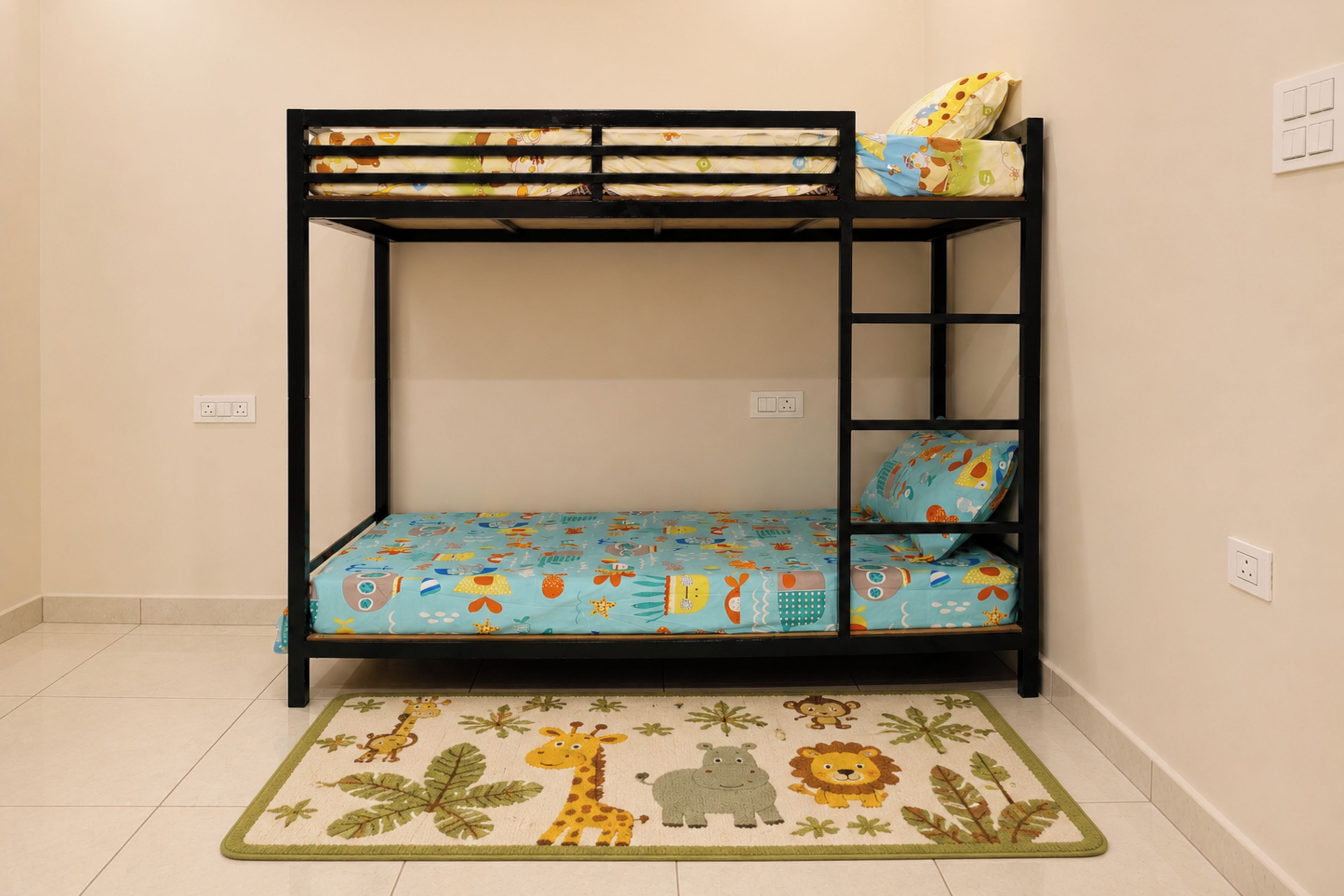A bunk bed with a blue mattress featuring animal prints, a matching pillow, and a green and yellow animal-themed rug on a tiled floor.