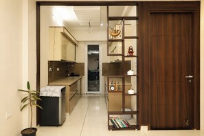 A kitchen with a refrigerator, sink, and a wooden cabinet. There is a potted plant and a shelf with books and decorative items. - Aarambh Hillside View (Dehradun)