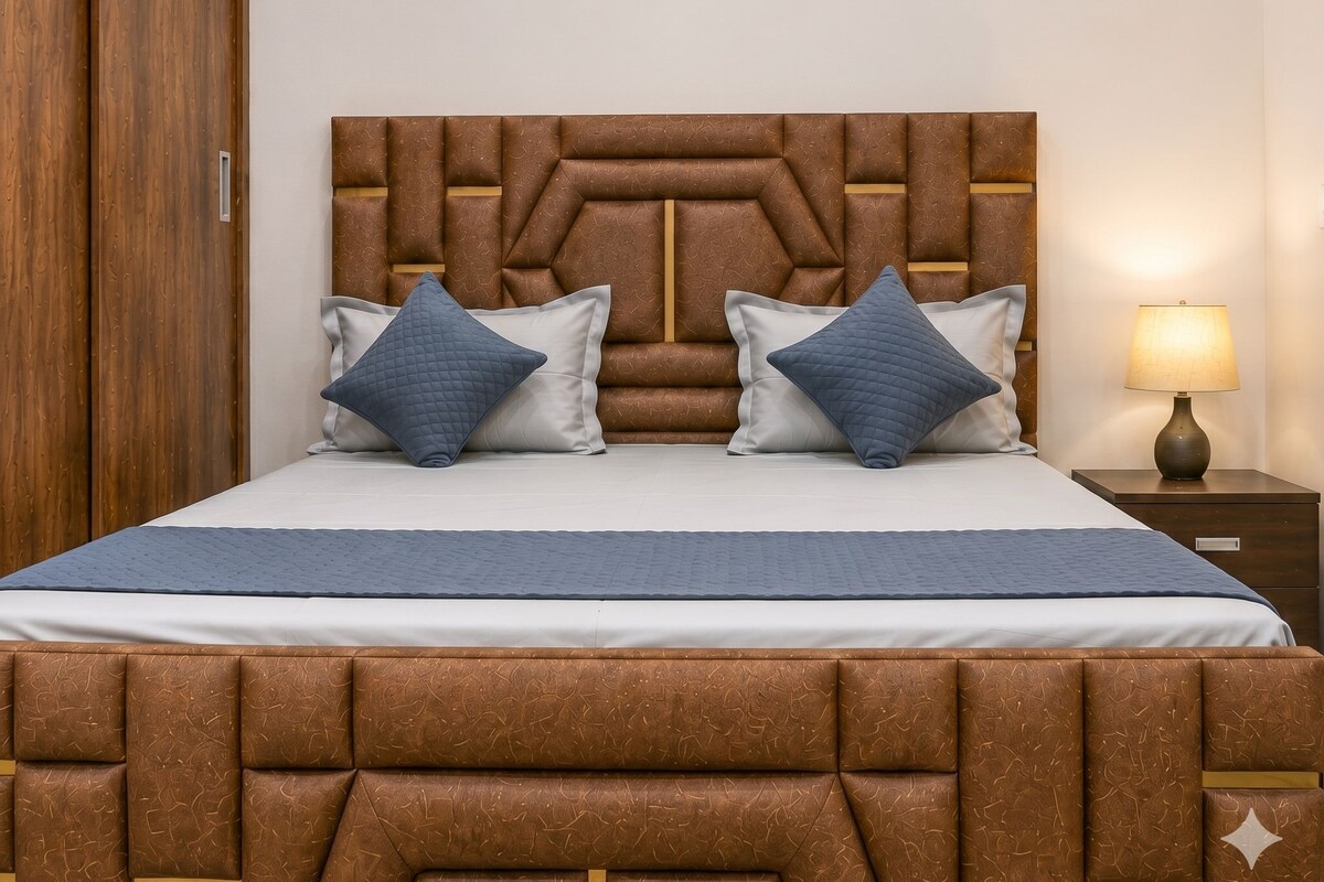 A bed with a headboard, two pillows, a bedside table with a lamp, and a wooden wardrobe.