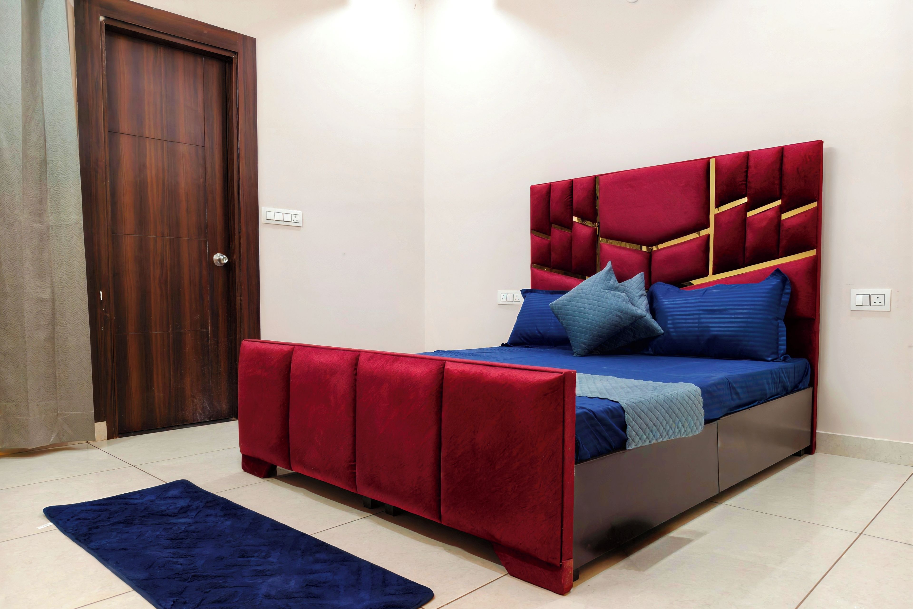 A bedroom with a bed, a red headboard, a blue bedspread, and a dark blue rug.