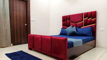 A bedroom with a bed, a red headboard, a blue bedspread, and a dark blue rug.