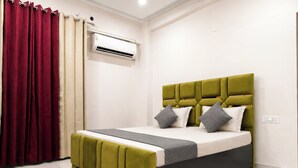 A room with a bed, curtains, an air conditioning unit, and a wall socket. - Aarambh Hillside View (Dehradun)