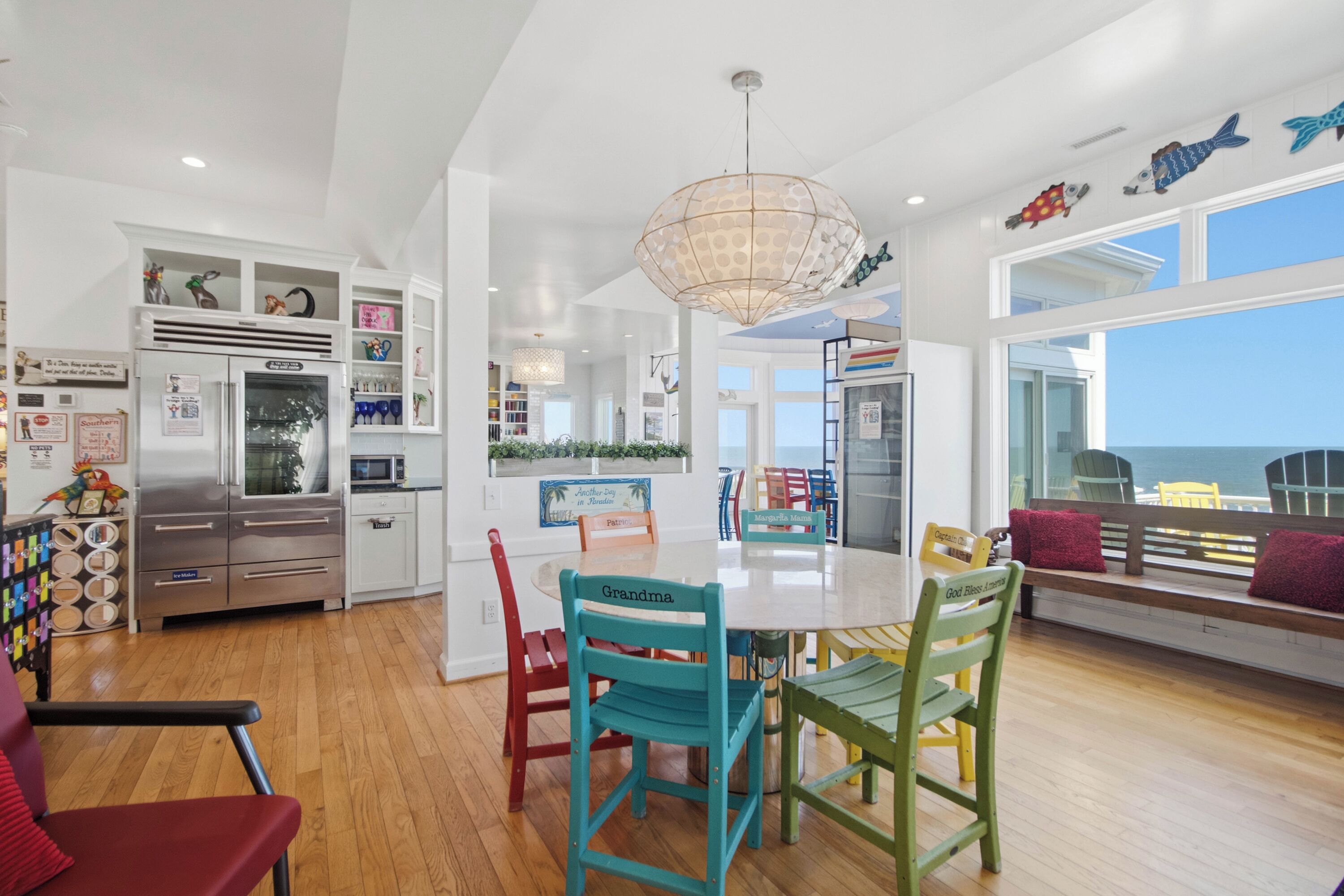 A modern kitchen with white cabinetry, a stainless steel refrigerator, and a dining area with a white table and colorful chairs.