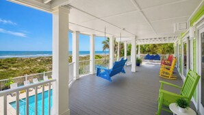 Eine überdachte Veranda mit Pool, Schaukelstühlen und Schaukelstuhlstühlen mit Blick auf einen Strand.