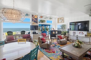 Een ruime woonkamer met een grote televisie, comfortabele zitmogelijkheden, een eettafel en uitzicht op de oceaan.