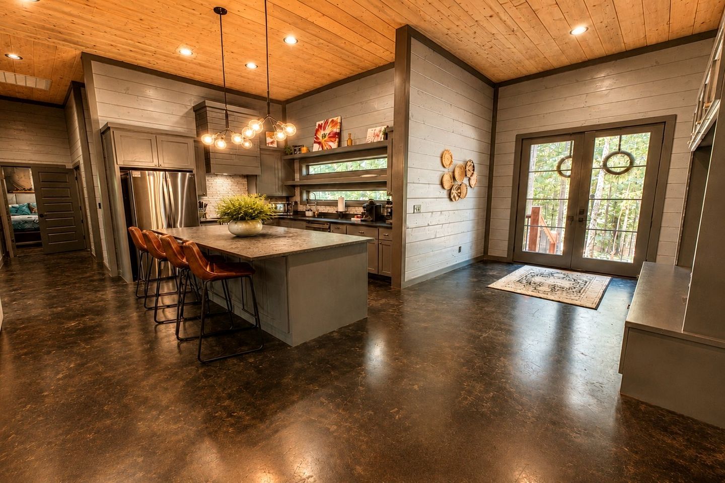 A modern kitchen with a central island, bar stools, and a large window.
