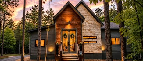 A cabin with a stone facade, a wooden front door, and a staircase leading to the entrance.