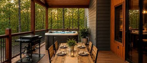 Une terrasse en bois avec un jacuzzi, une table à manger et des chaises, le tout entouré d’arbres.