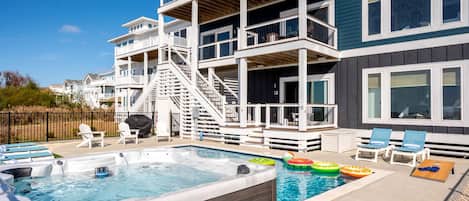 A multi-story building with a swimming pool, outdoor seating, and a covered deck area.