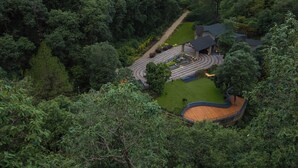 Une maison entourée d’une forêt dense, avec une allée sinueuse menant à une terrasse en bois.