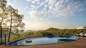 Una piscina amb terrassa de fusta, envoltada d'arbres i vista a un turó boscos.