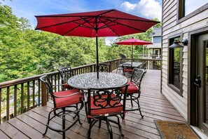 Eine Holzterrasse mit einem runden Tisch, Stühlen und zwei roten Sonnenschirmen, sowie einem Metallgeländer.