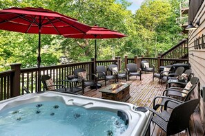 A hot tub surrounded by outdoor furniture on a wooden deck with red umbrellas. - Deluxe Cabin with Three Stunning Decks for a Group Getaway on Norris Lake, Tennessee (Speedwell)