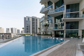 A modern building with a rooftop swimming pool, multiple balconies, and a cityscape in the background. - Stylish New 1 bedroom with Private Jacuzzi -Binghatti (Dubai)