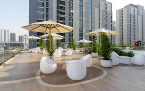 A rooftop terrace with modern seating, potted plants, and large umbrellas. - Stylish New 1 bedroom with Private Jacuzzi -Binghatti (Dubai)