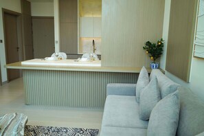 A modern kitchen with a built-in island, a grey sofa, and a small potted plant. - Stylish New 1 bedroom with Private Jacuzzi -Binghatti (Dubai)