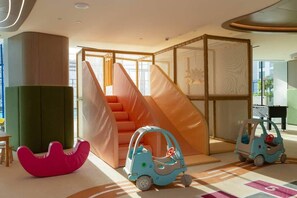 Ein Kinderspielbereich mit weichen Sitzgelegenheiten, einer Rutsche und Spielzeugautos.