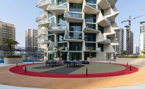 A modern building with a unique zigzagged facade, outdoor seating area, and surrounding high-rise buildings. - Stylish New 1 bedroom with Private Jacuzzi -Binghatti (Dubai)