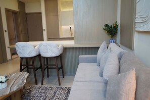 A modern living room with a sofa, two bar stools, a small table with a vase, and a patterned rug. - Stylish New 1 bedroom with Private Jacuzzi -Binghatti (Dubai)