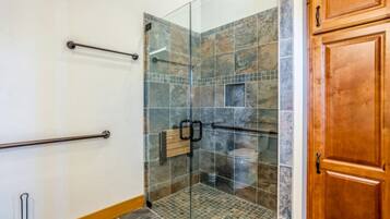 A glass-enclosed shower with a tiled floor, a wooden door, and a metal grab bar on the wall.