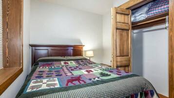 A bedroom with a wooden headboard, a quilt with various patterns, a bedside lamp, and a wooden wardrobe.