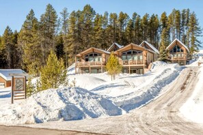 Eine Lodge mit mehreren Holzhütten, einem verschneiten Hang und blauem Himmel.