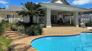 Uma casa com varanda coberta, piscina e uma palmeira.