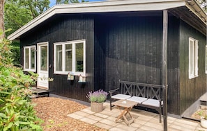 Ein schwarzes Holzgebäude mit drei Fenstern, einer Bank und einem kleinen Tisch mit einem Blumentopf.