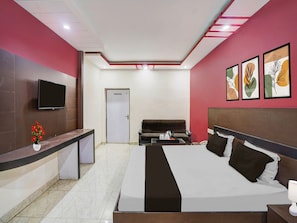 A hotel room with a bed, a desk, a television, and a door. - Classic Hotel Shantila Inn (Prayagraj)