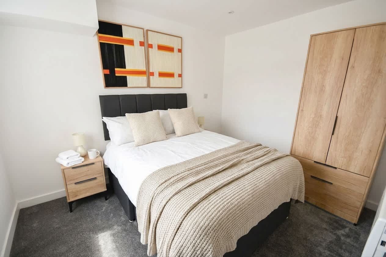 A bedroom with a bed, nightstand, wardrobe, and abstract wall art.