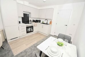Une cuisine moderne avec des meubles blancs, un coin repas avec une table dressée pour deux personnes et un tapis gris.