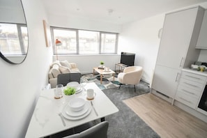 A modern living space with a dining area, sofa, TV, and kitchen.