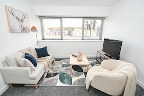 Ein modernes Wohnzimmer mit einer Couch, einem Sessel, einem Couchtisch und einem Fernseher.