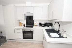 Une cuisine moderne avec des meubles blancs, un four encastré, une machine à café et un évier doté d’un robinet noir.