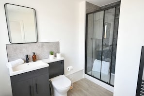 A modern bathroom with a white sink, dark cabinets, a toilet, and a glass shower enclosure.