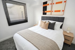 A bedroom with a bed, a nightstand, a lamp, and a window with blinds.