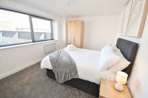 Ein Schlafzimmer mit einem Bett, einem Nachttisch, einer Lampe und einem Fenster mit Jalousien.