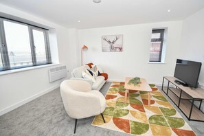 Een moderne woonkamer met een bank, een salontafel, een televisie en een groot raam met zonwering.