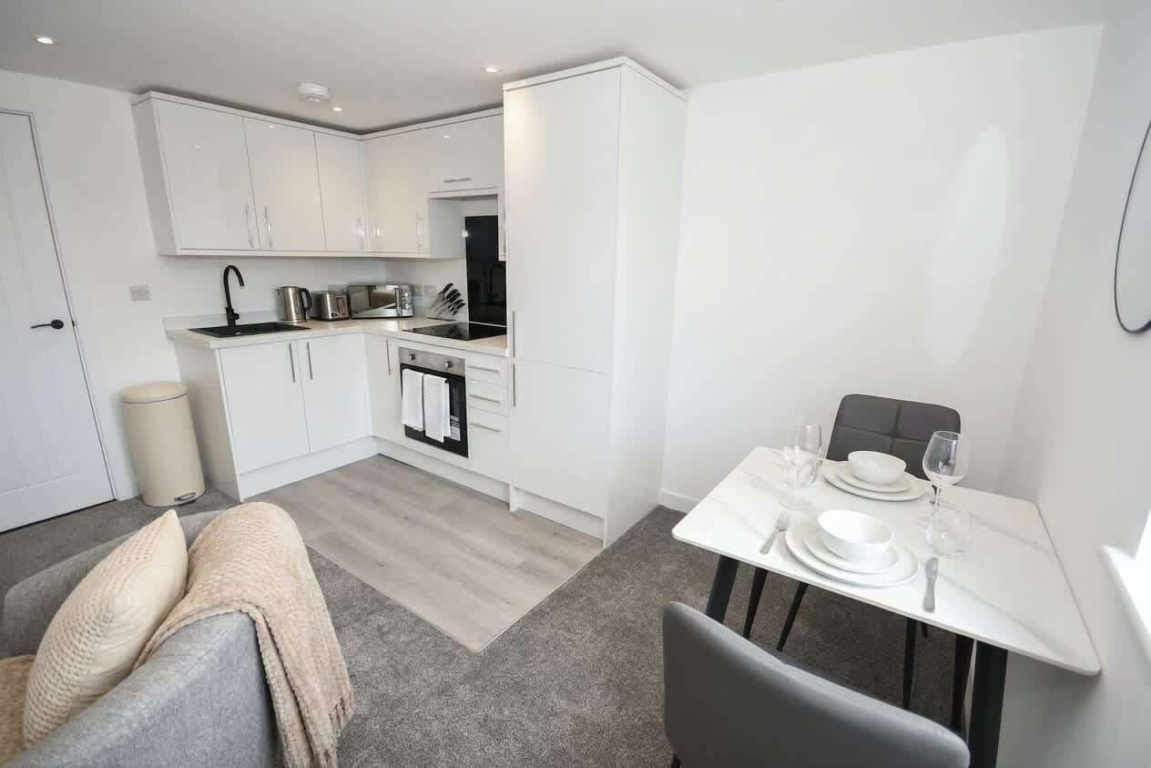 A modern kitchen with white cabinetry, a dining table set for two, and a grey sofa with a blanket.