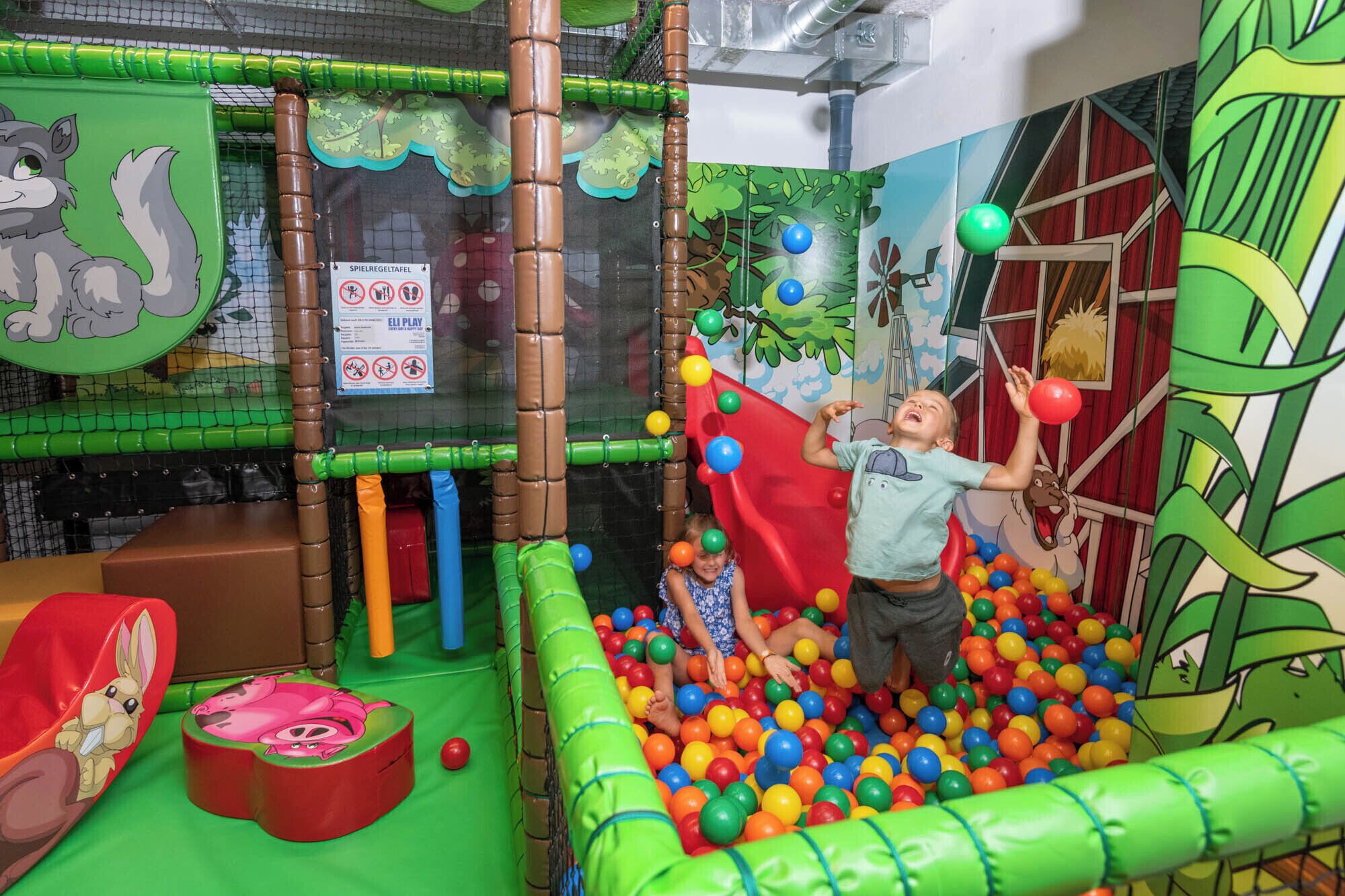 Un área de juegos con piscina de pelotas, estructuras para escalar y decoraciones con personajes de caricaturas.