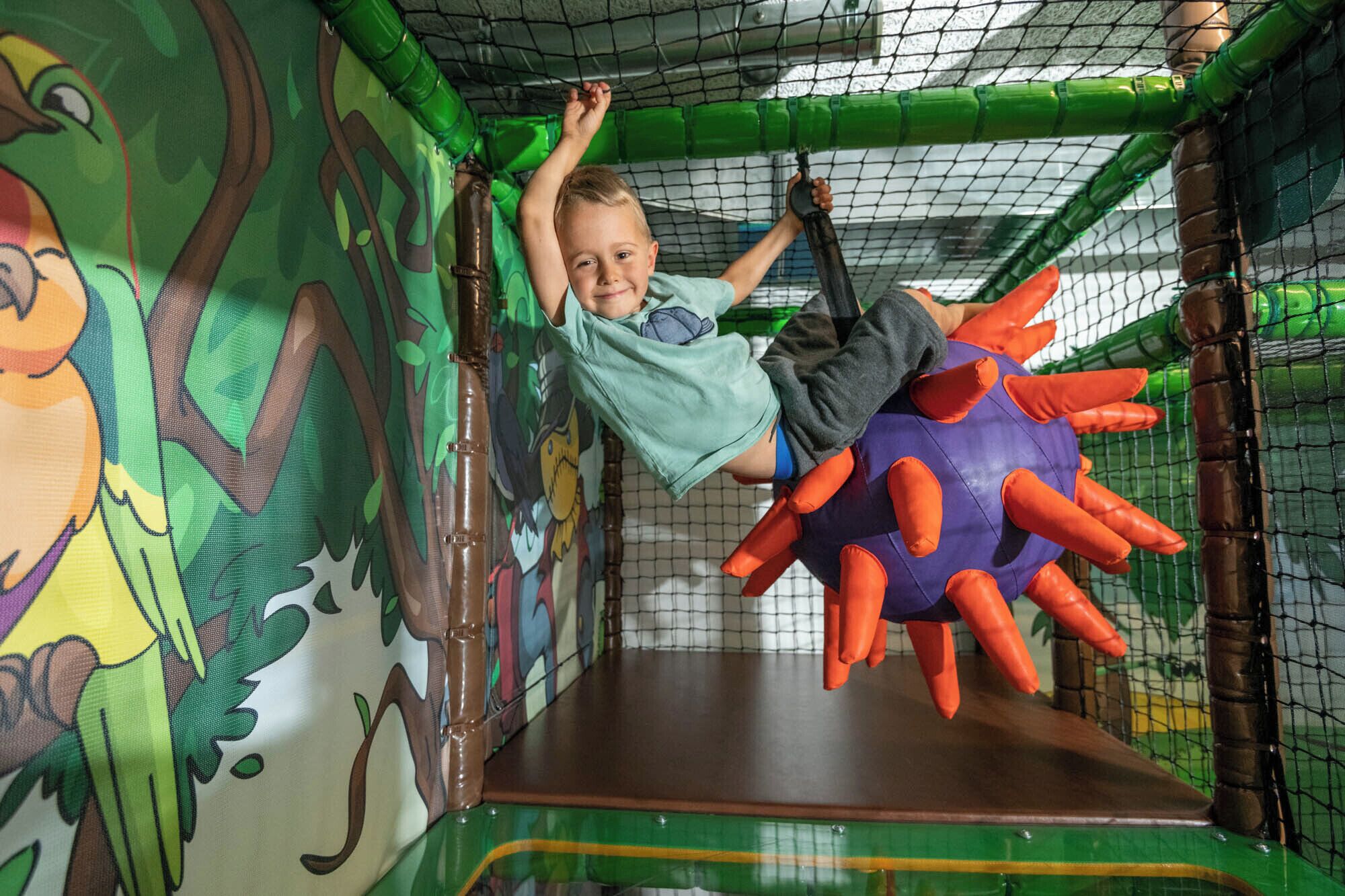 A child climbing on a play structure with a colorful wall and netting.