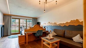 Una habitación con un escritorio de madera, un sofá, una silla y un ventanal con vistas a un edificio y un paisaje.